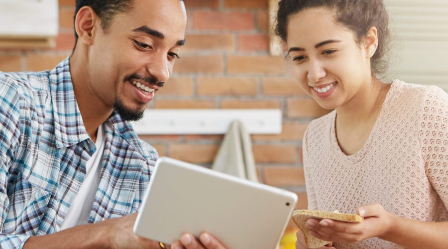 People, family, online shopping concept. Young affectionate couple going to buy new accomodation, look at advertisments in internet, use modern tablet computer, preparre lunch together. Home interior